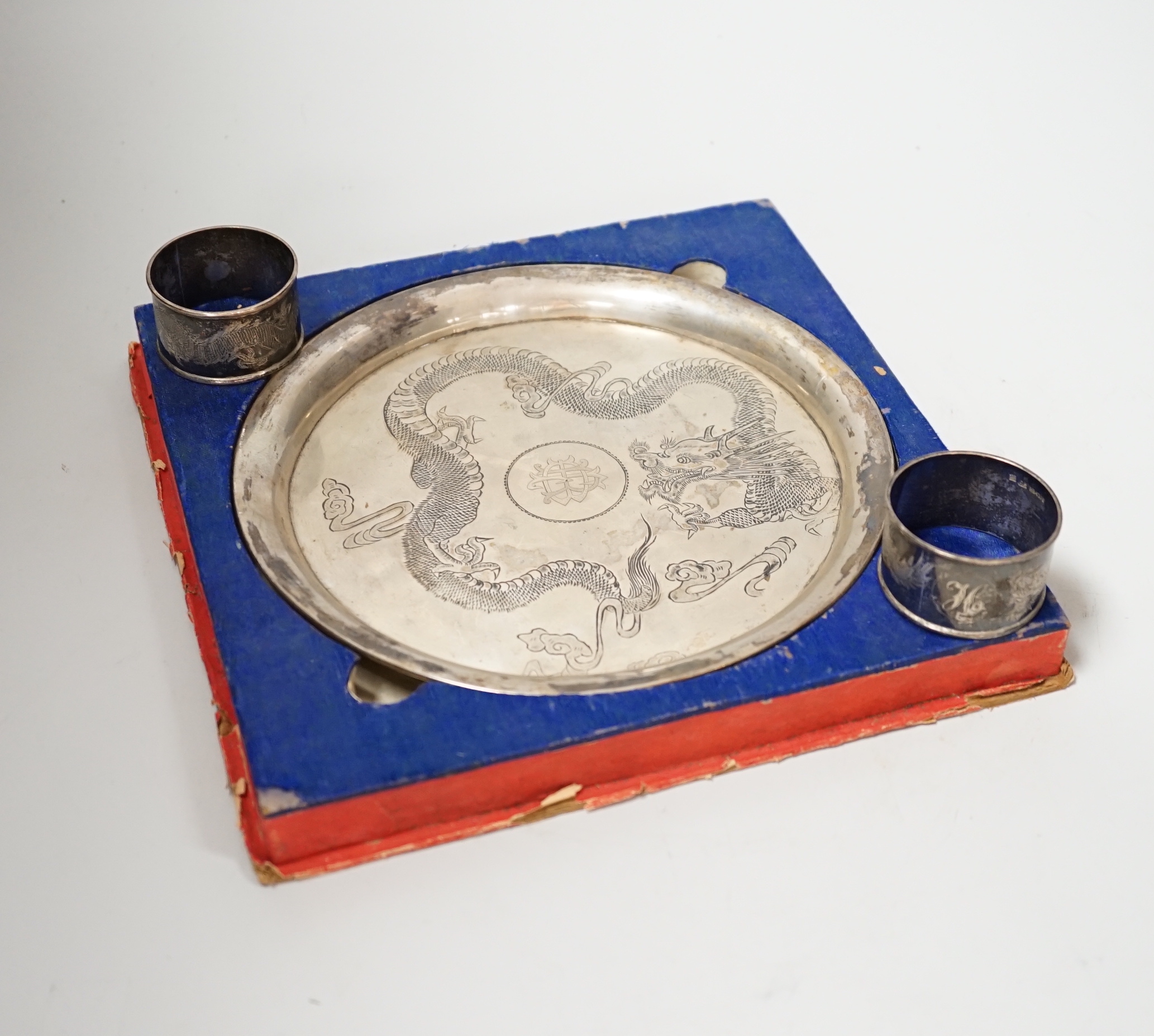 A Chinese white metal ‘dragon’ salver, late 19th century, 20.2cm carded silk box base and two similar napkin rings.